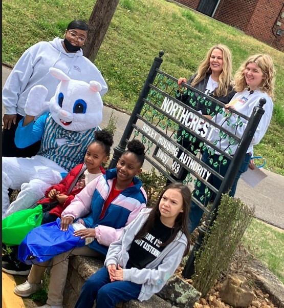 A group of women and girls sitting by the Ripley Housing Authority Northcrest sign with a person in an Easter bunny costume.