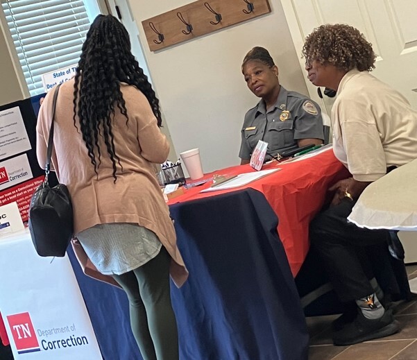A lady standing at the Department of Corrections display table talking to two women sitting behind the table.