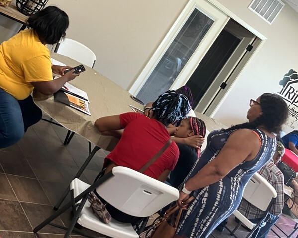 Four people sitting at a table and one lady standing up behind some of them.