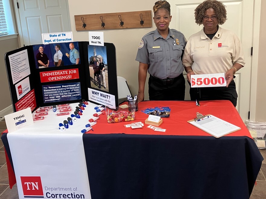 Two ladies standing behind the table with the Tennesee Department of Corrections display for the job fair.