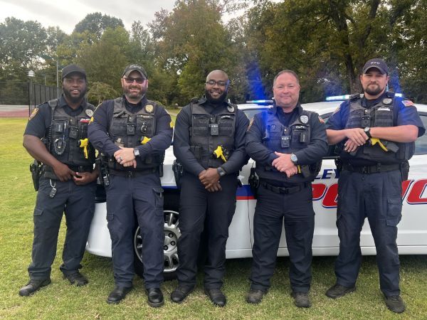 Five policemen stand against a police cruiser, and smile for a picture