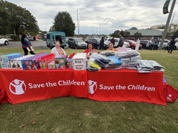 Three women behind the save the Children table, that is full of goodies.