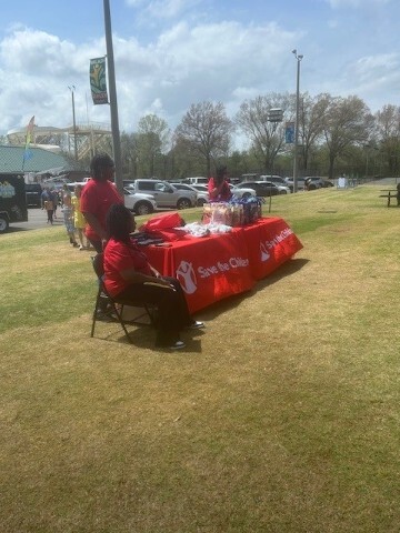 Table is sitting outside with three people around it with promotional merchandise on it. 