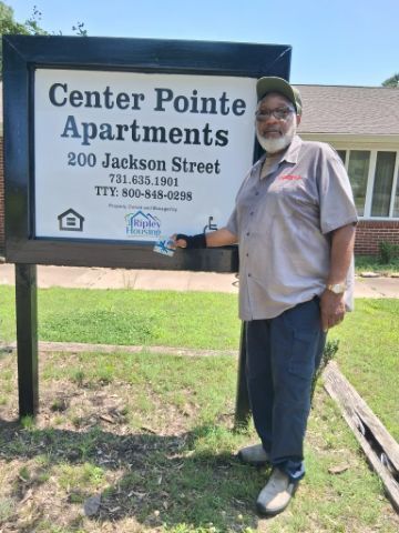 A man stands next to the Center Pointe Apartments sign holding the gift card he won.