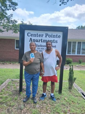 A man and woman holding hands in front of the Center Pointe Apartments sign holding the gift card they won.