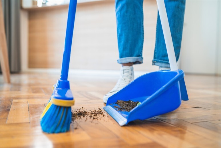 A close up of a broom sweeping dirt off of a floor into a dustpan.
